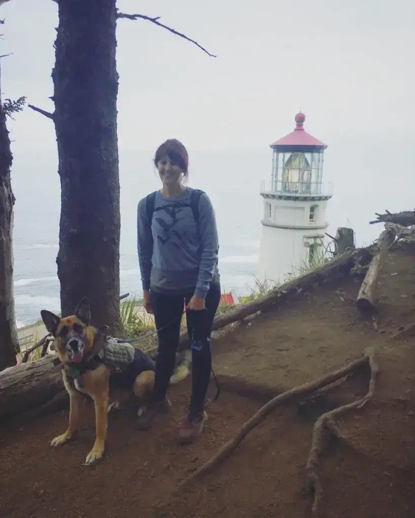 Woman and German Shepherd Dog on a hike standing in front of a lighthouse.