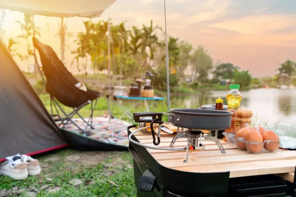 Camp site with a tent, chairs, and table with cooking food.