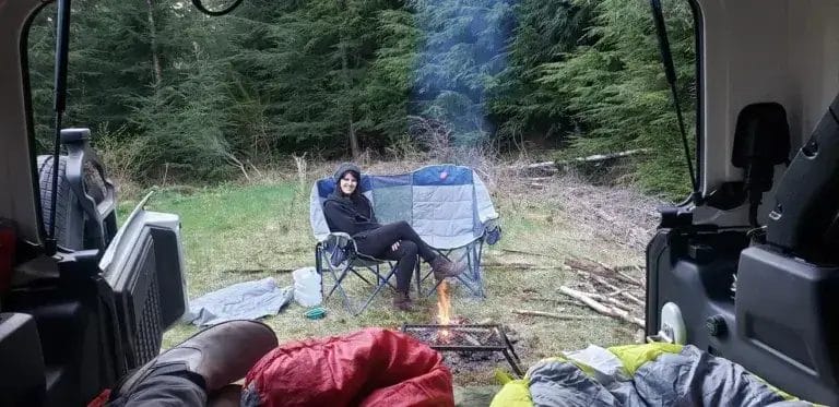 Woman sitting on a camp chair next to a camp fire looking into a Jeep Wrangler.
