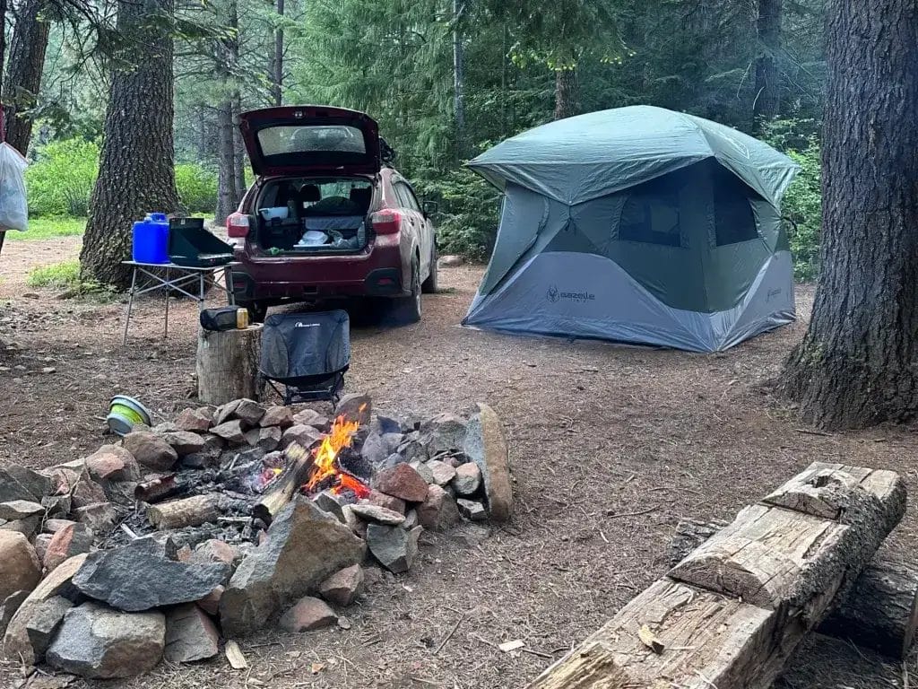 Campsite with a fire pit, parked Subaru Crosstrek and a Gazelle tent.