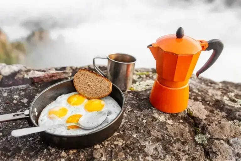 Fried eggs in a pan and coffee geyser maker outdoors in the mountains.