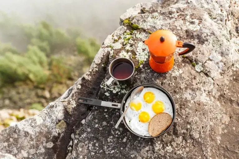 breakfast meal: Fried eggs in a pan and coffee geyser maker outdoors in the mountains.
