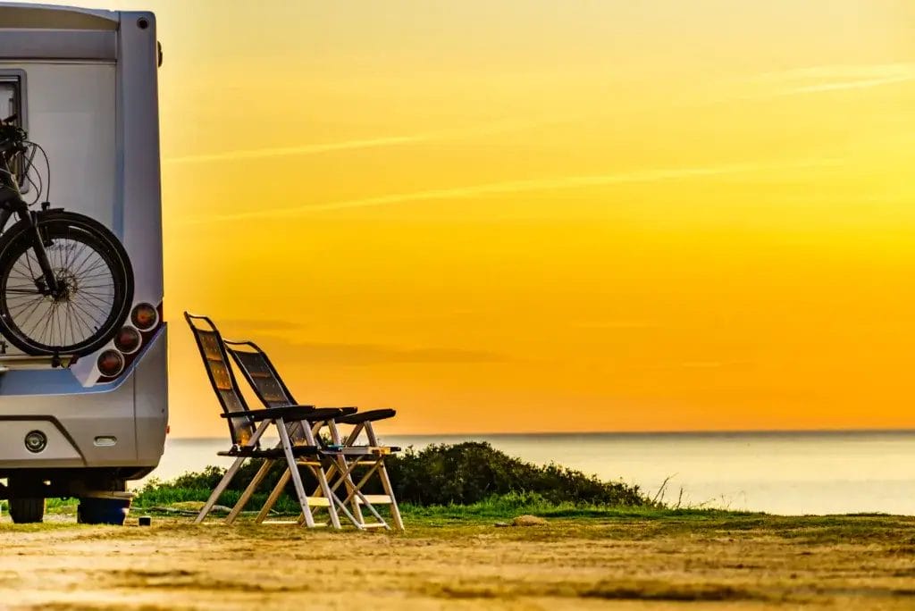 Camper vehicle and tourist chairs on spanish sea coast. Camping on seaside. Holidays and travel with motor home.