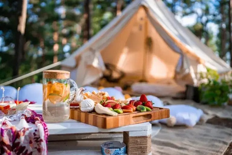 Beautiful white decor in boho style. Picnic in the nature, table, carpets, wigwam, tent, pillows camping.
