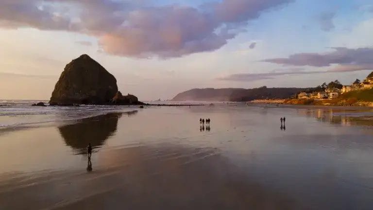 People walk on the beach reflection late afternoon at dusk in Cannon Beach Oregon.