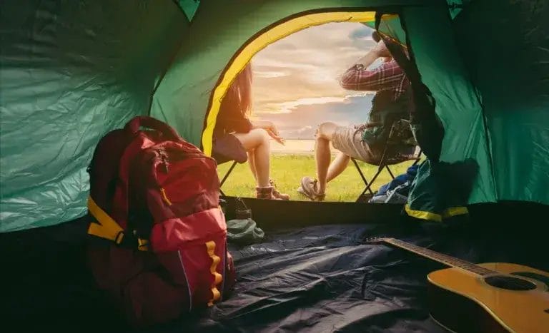 Couple camping together in forest with a tent, backpack, guitar and mountain view.