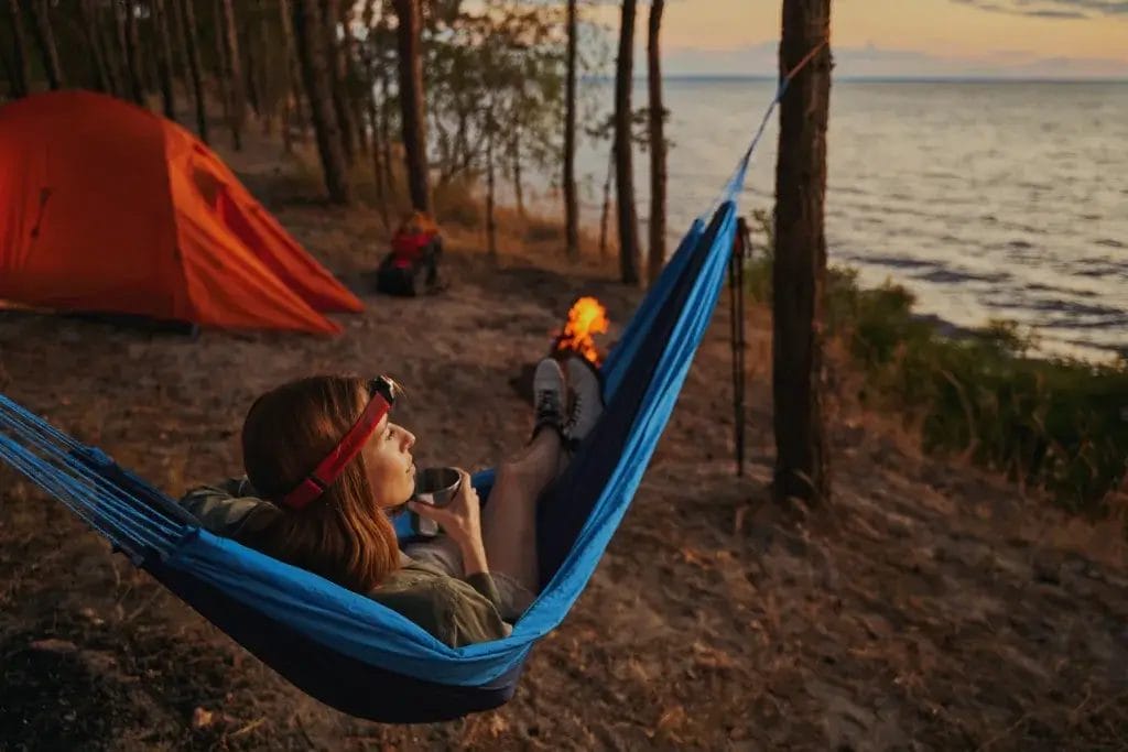 Caucasian tourist resting in hammock at the campsite while watching the sky over lake in twilight.