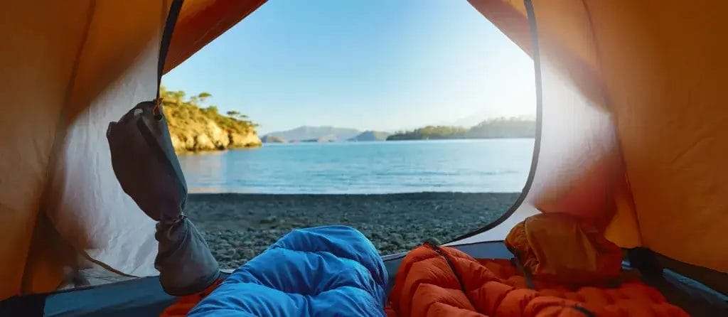 Two people travelers lying in tent in sleeping bags with view at wild tropical beach.
