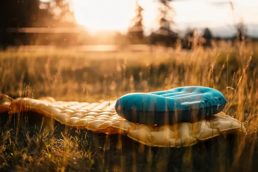 Camping bed ideas - inflatable pad and camping pillow laying on the grass at sunset.