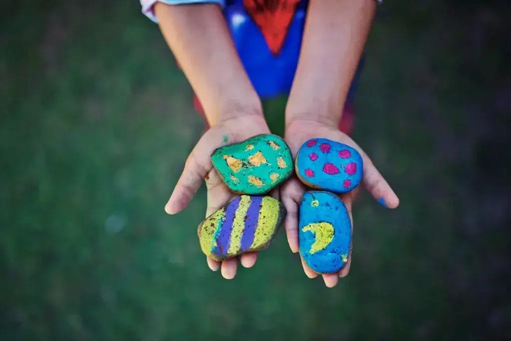 Child showing camping crafts, painted stones.