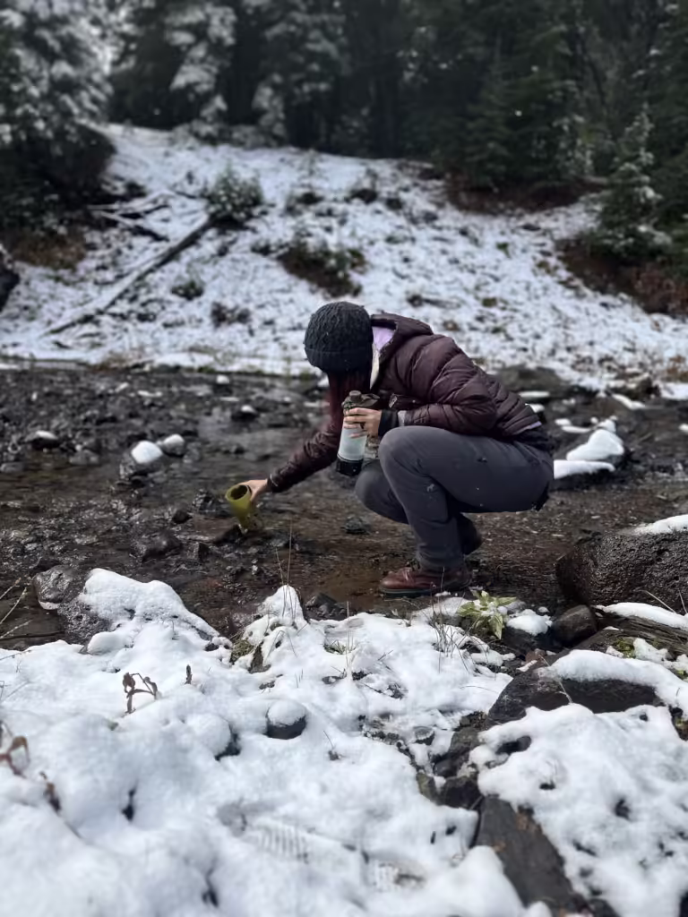 Woman filling up a water bottle from a snowy stream