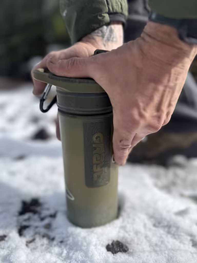 Two hands on a GRAYL water purifying bottle in the snow.