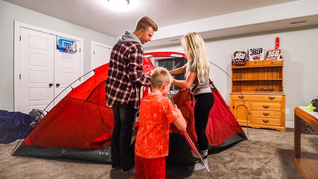 Father and daughters setting up a tent in the living room for indoor camping.