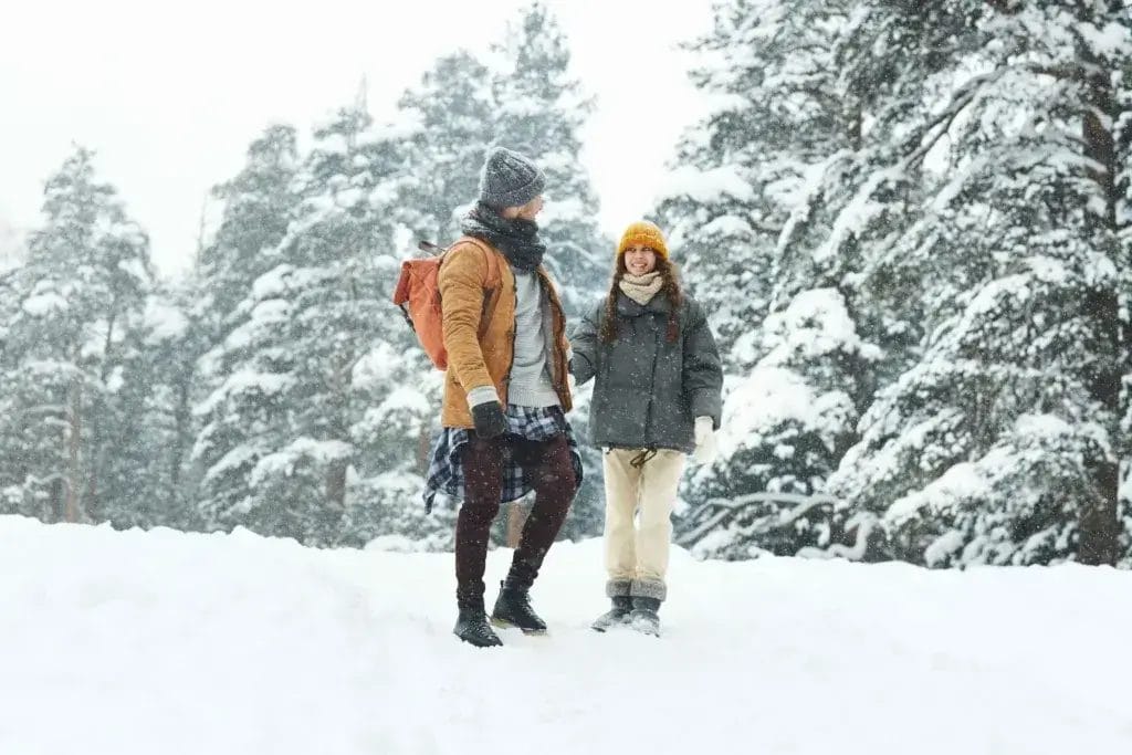 Man and woman hiking in the snow with snowy pines in the background.