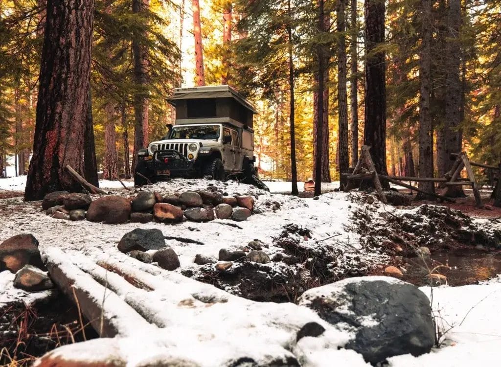 Jeep Gladiator with a popup tent in a snowy forest setting.