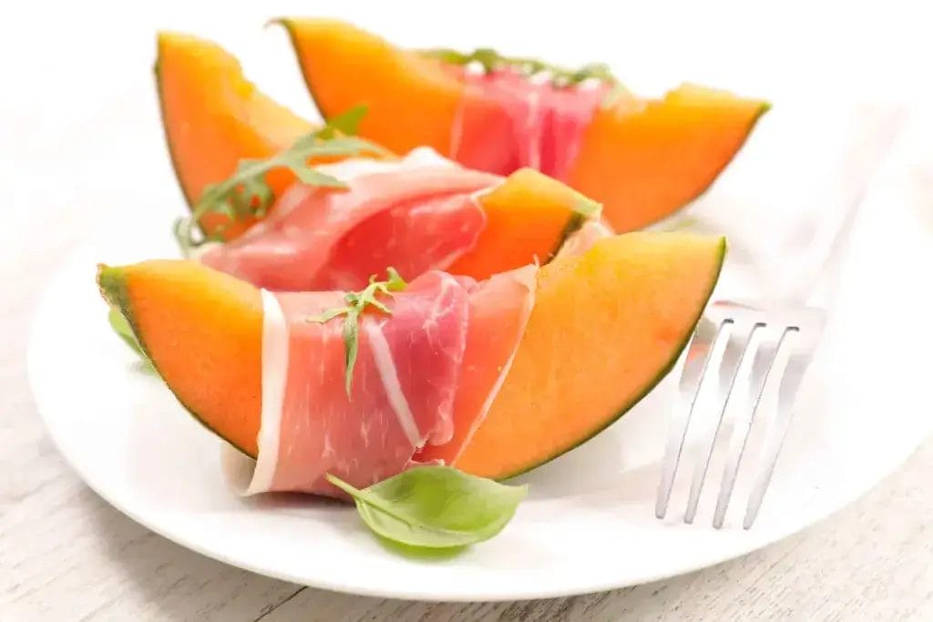 Prosciutto and melon on a white plate.