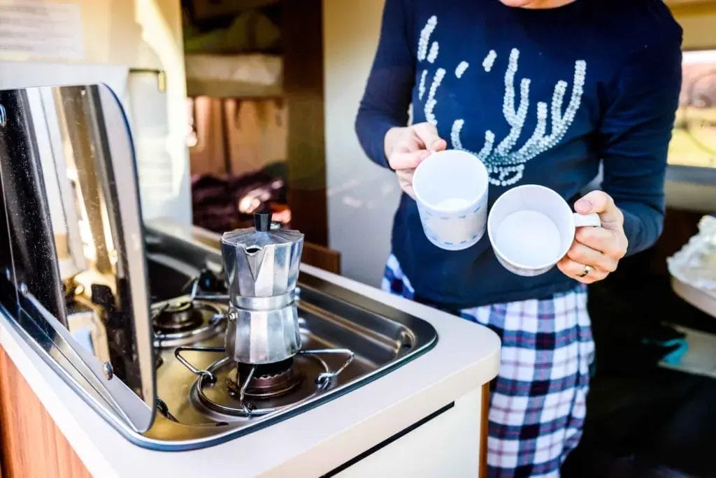 Woman making coffee holding two cups inside of an RV.