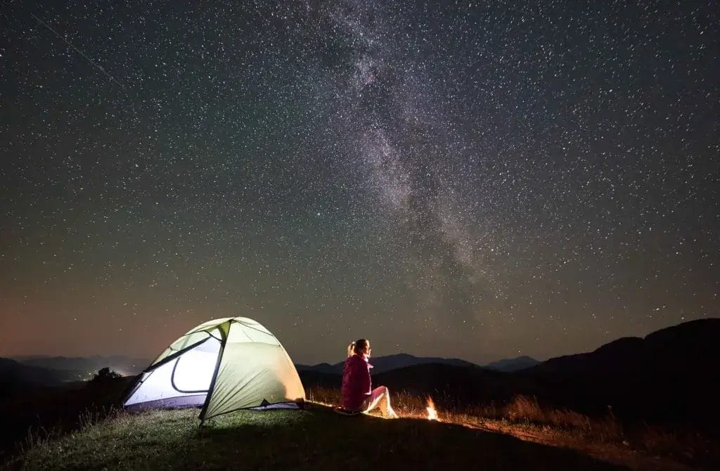 Woman solo camping under a starry sky with a campfire.