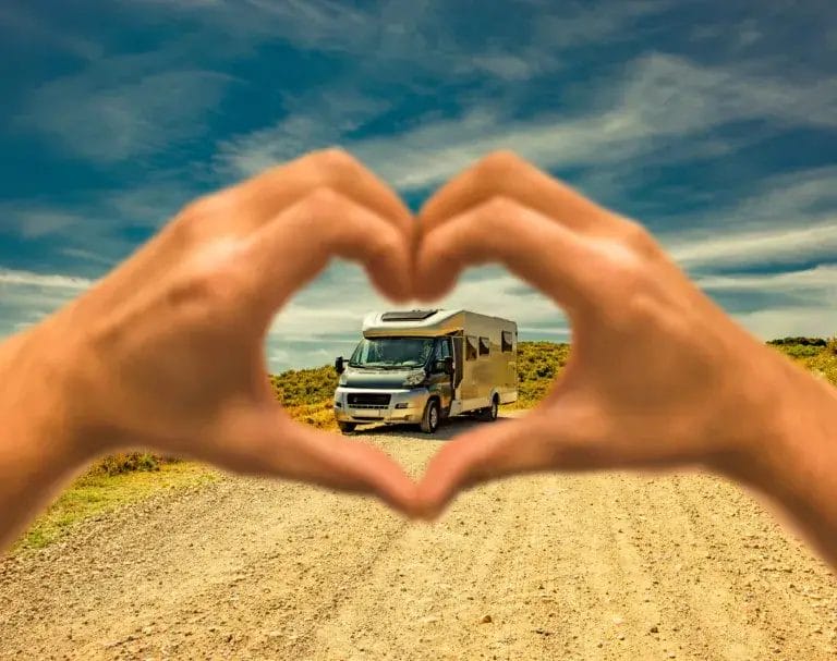 Hands forming a heart shape around RV camper in the background.