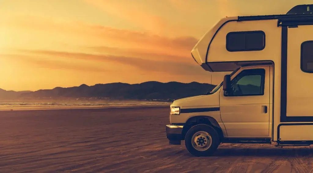 Motor home in the sand with an orange sunset in the background.