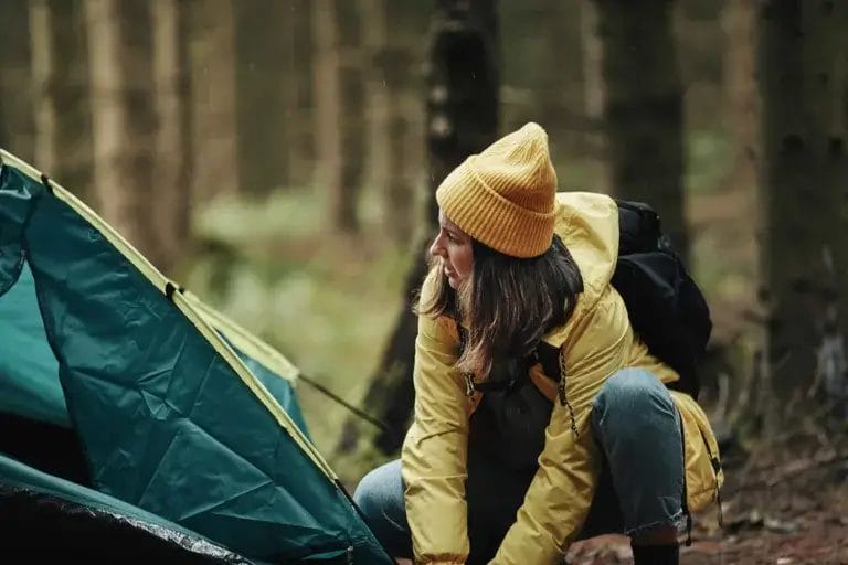 Young woman next to a tent solo camping in the forest.