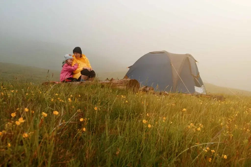 Woman and child sitting in a field with a tent on a rainy day.