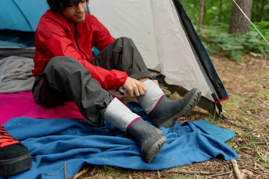 Man in a tent putting on rain boots.