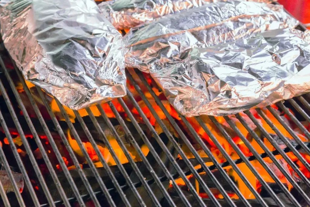 Two foil packs cooking on a grill.