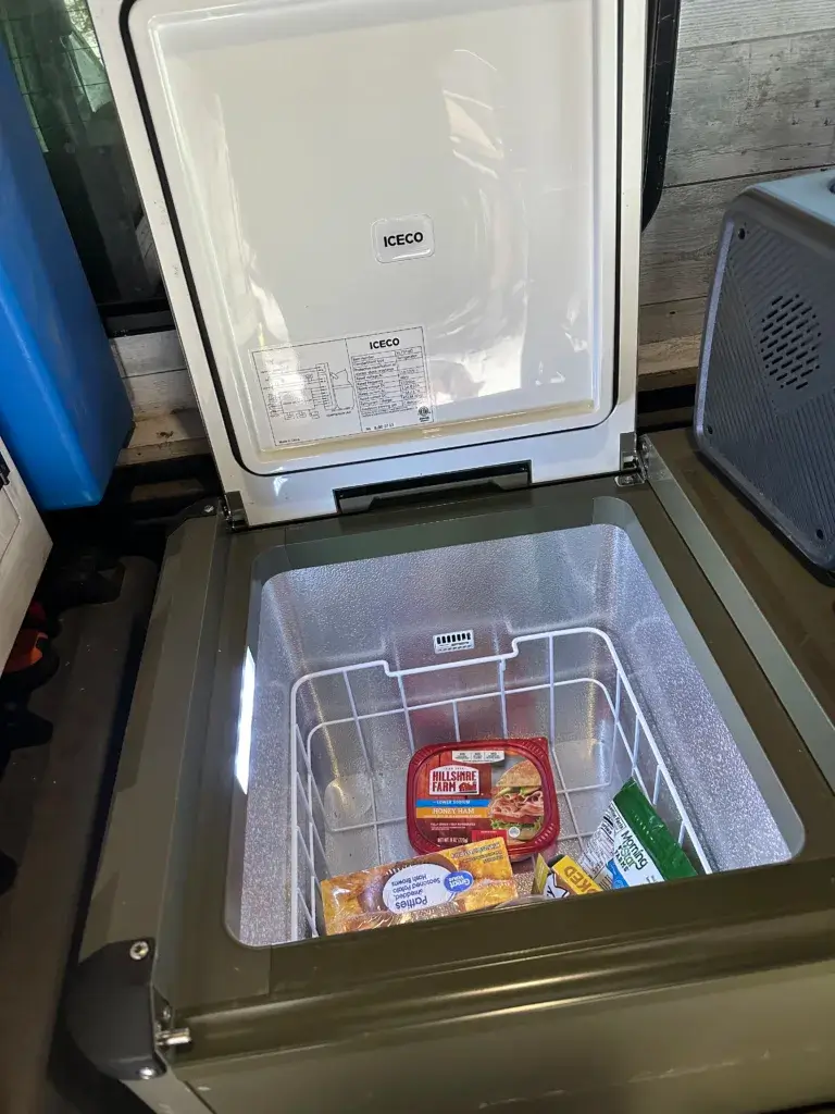 Green Icedo refrigerator with one side open containing some lunch meat and hashed browns.
