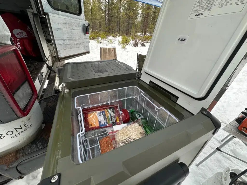 Iceco refrigerator sitting on a table at camp with one side open.