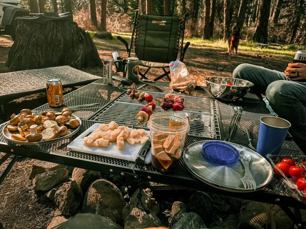 AroundFire fire pit in a camp setting with friends grilling kebabs and vegetables.