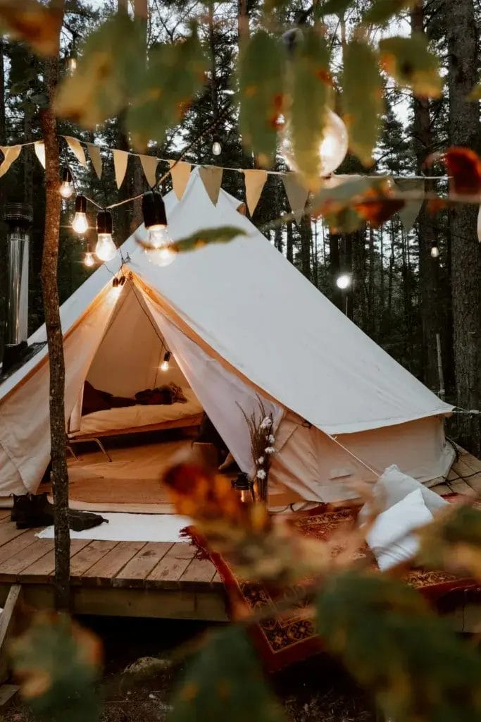 A cozy glamping tent amidst forest trees decorated with warm lights for a relaxing camping experience.