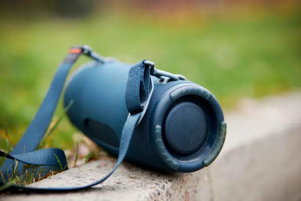 Blue portable bluetooth speaker sitting on a curb.