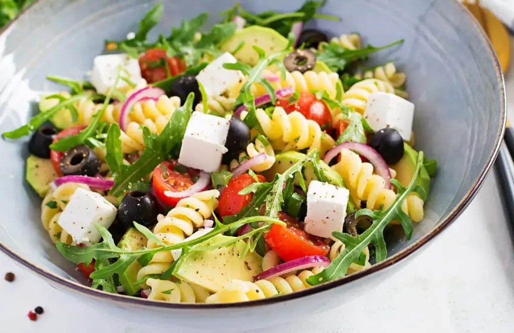 Pasta salad with tomato, avocado, black olives, red onions and cheese feta. Mediterranean cuisine.