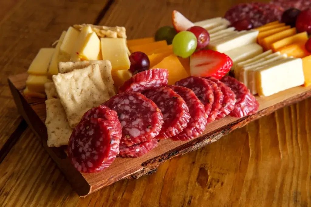 Italian charcuterie board featuring crackers cheese and salami served on wooden plank with raw bark edge