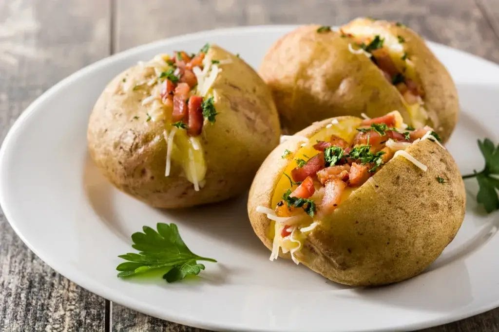 Stuffed potatoes with bacon and cheese on plate on wooden table. Close up