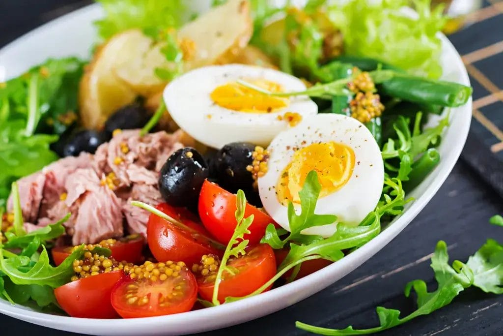 Healthy hearty salad of tuna, green beans, tomatoes, eggs, potatoes, black olives close-up in a bowl on the table. Salad Nicoise. French cuisine.