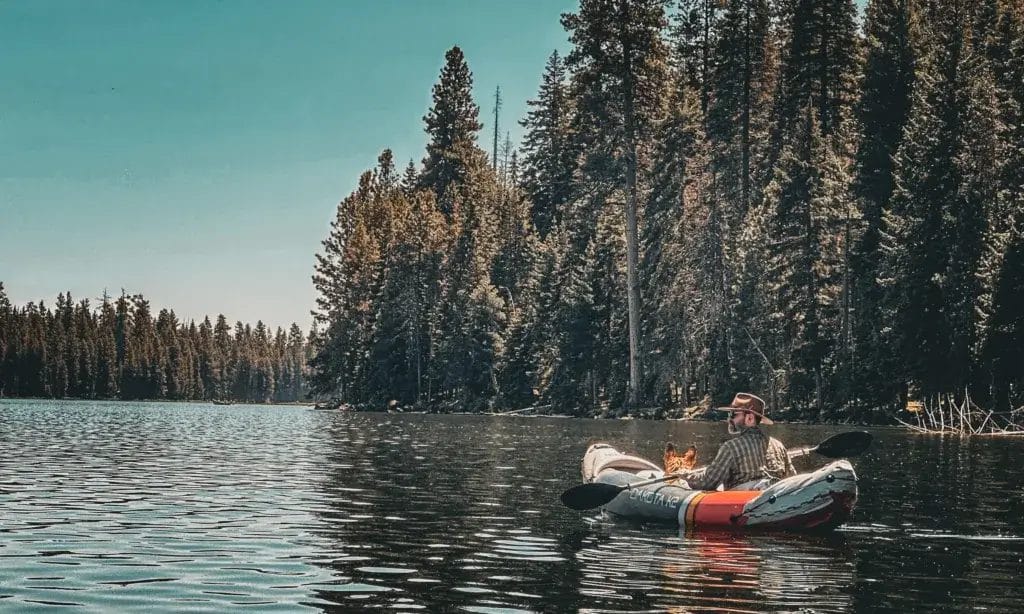 Man in an inflatable kayak on the river with a German Shepherd.
