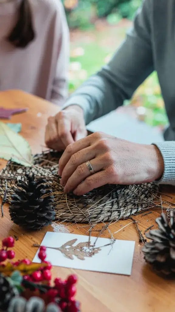 A family making crafts with dried leaves, twigs, and pinecones at a table.