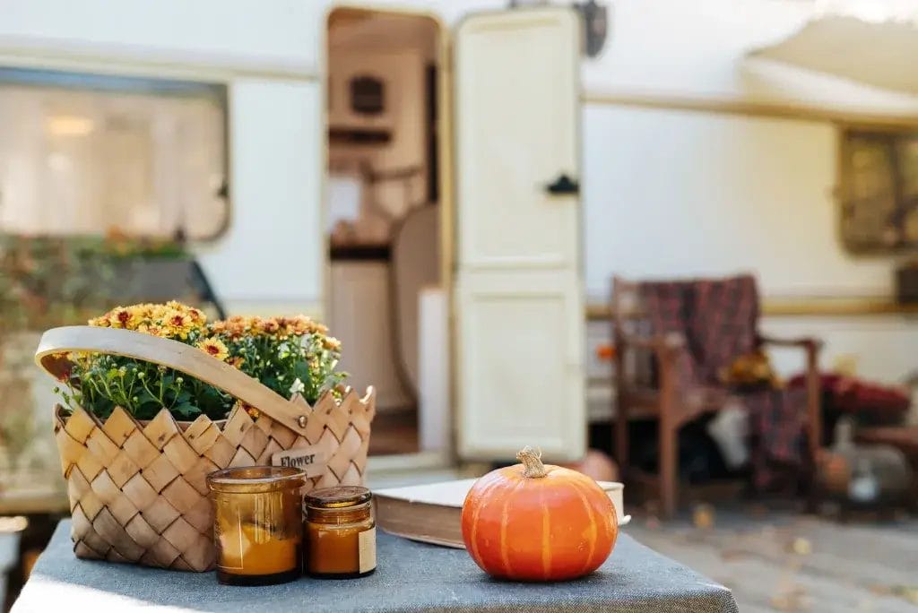 RV in the background and a picnic table with a mini pumpkin, scented candles and a basket with flowers.