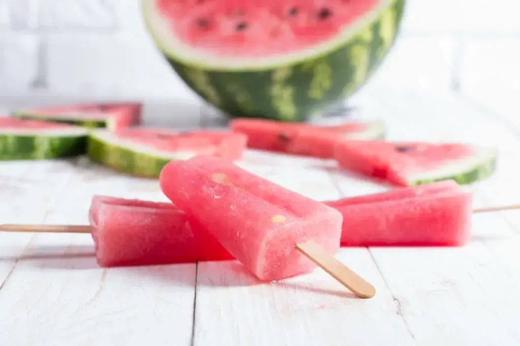 Watermelon popsicles on a white wooden table.