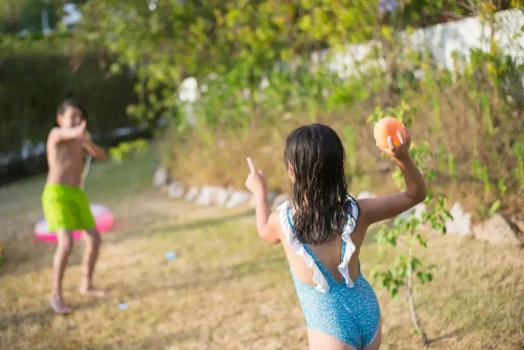 Children having fun with a water balloon fight in a sunny garden setting, enjoying the summer day.