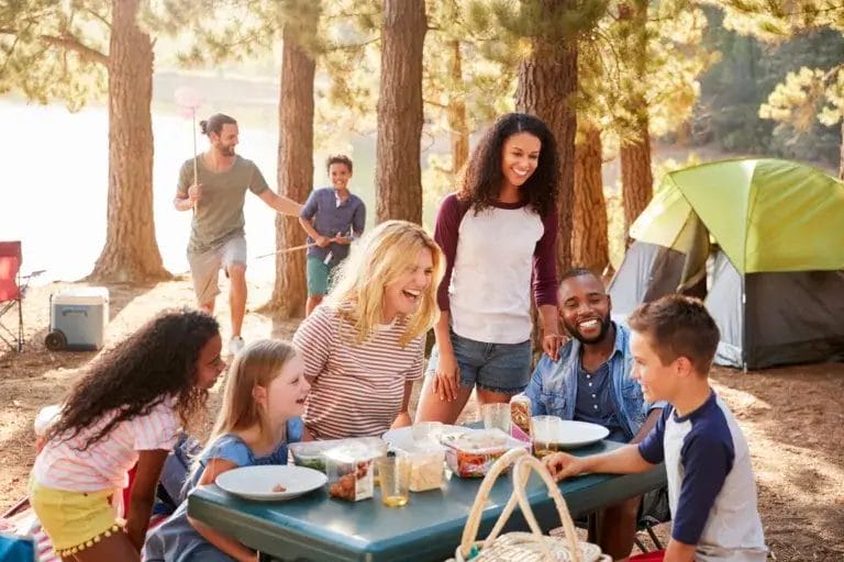 Family and friends ona camping trip sitting around a table laughing and enjoying a meal.