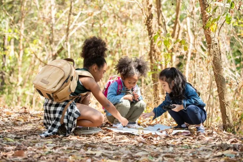 Three children are sitting in the leaves, looking at a map on a camping trip.