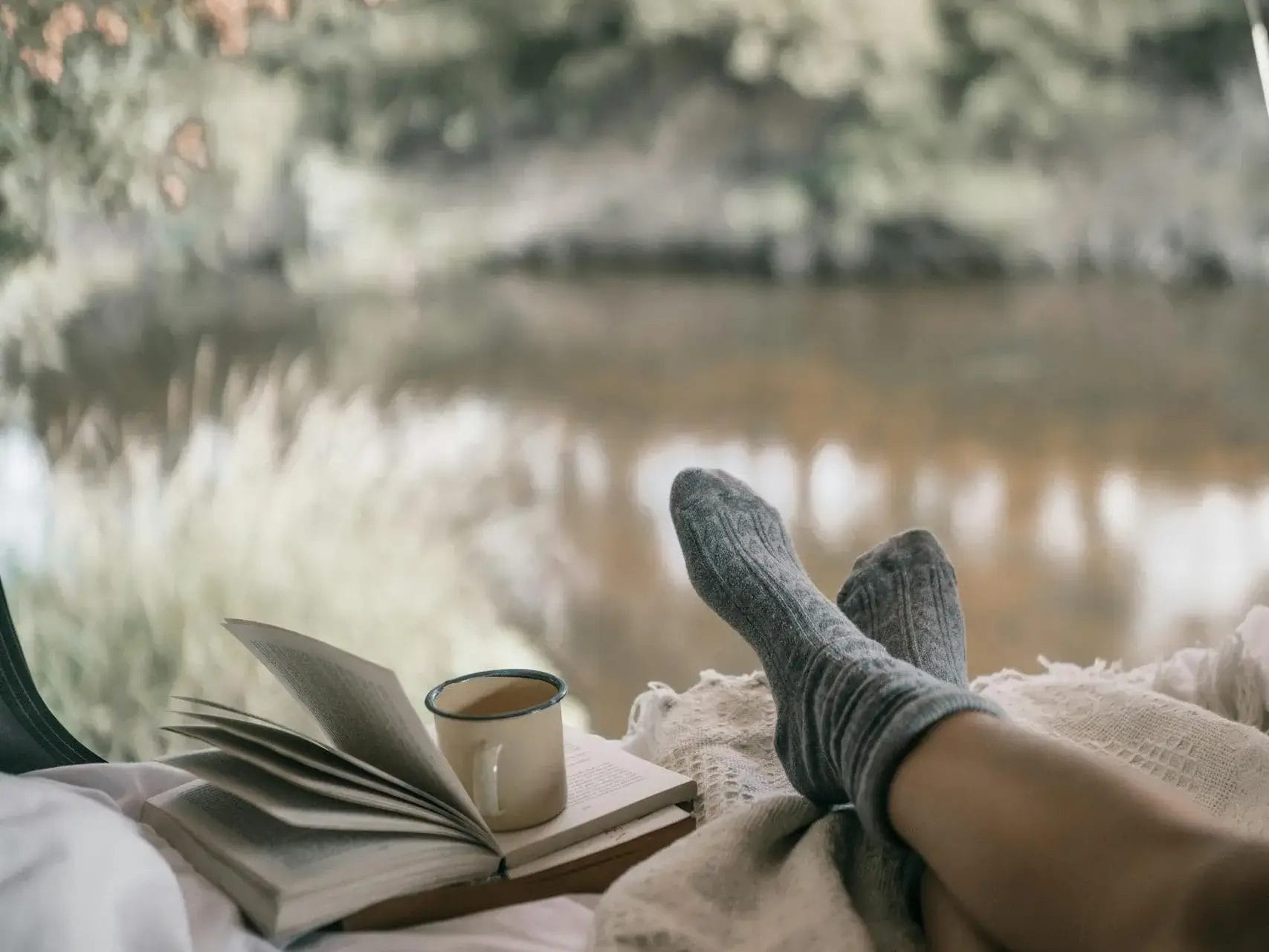 Relax in a tent with a book and coffee by a tranquil lake.