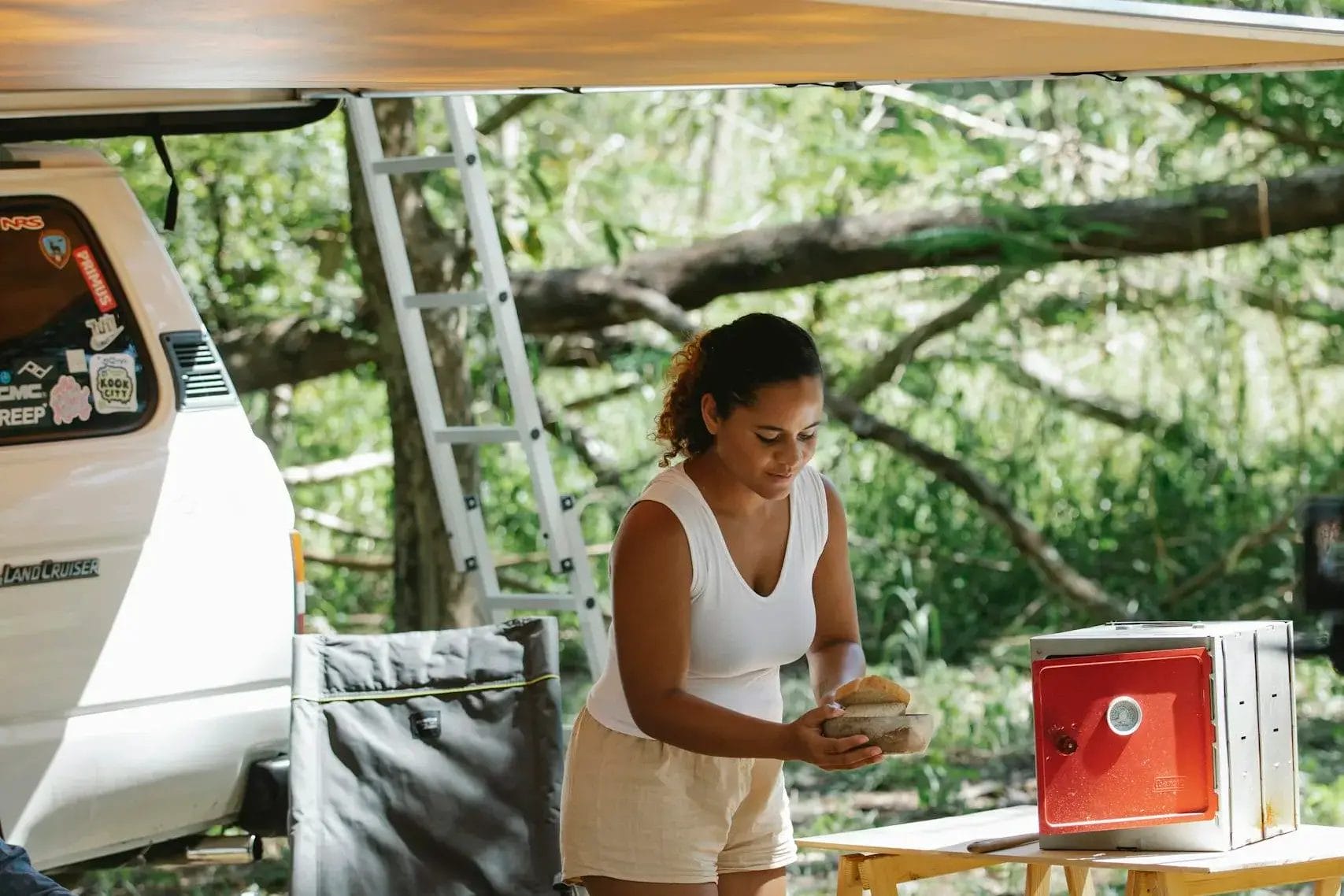Woman enjoying outdoor camping with portable oven, surrounded by nature.