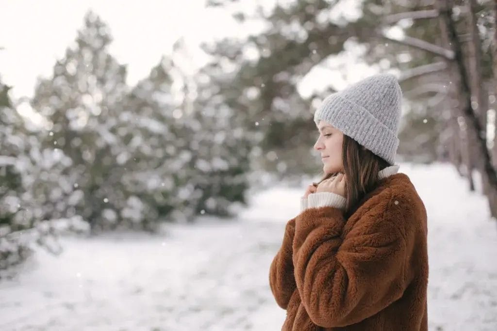 Woman in the snow wearing a cozy warm sweater and beanie hat.