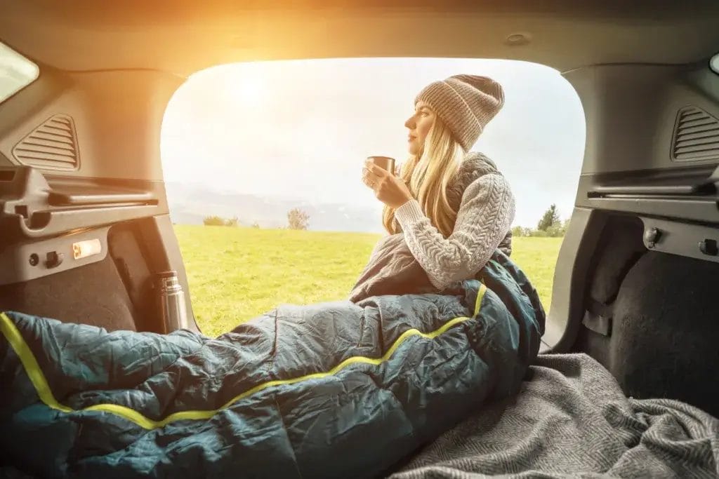 Woman in a sleeping bag car camping on a winter day.