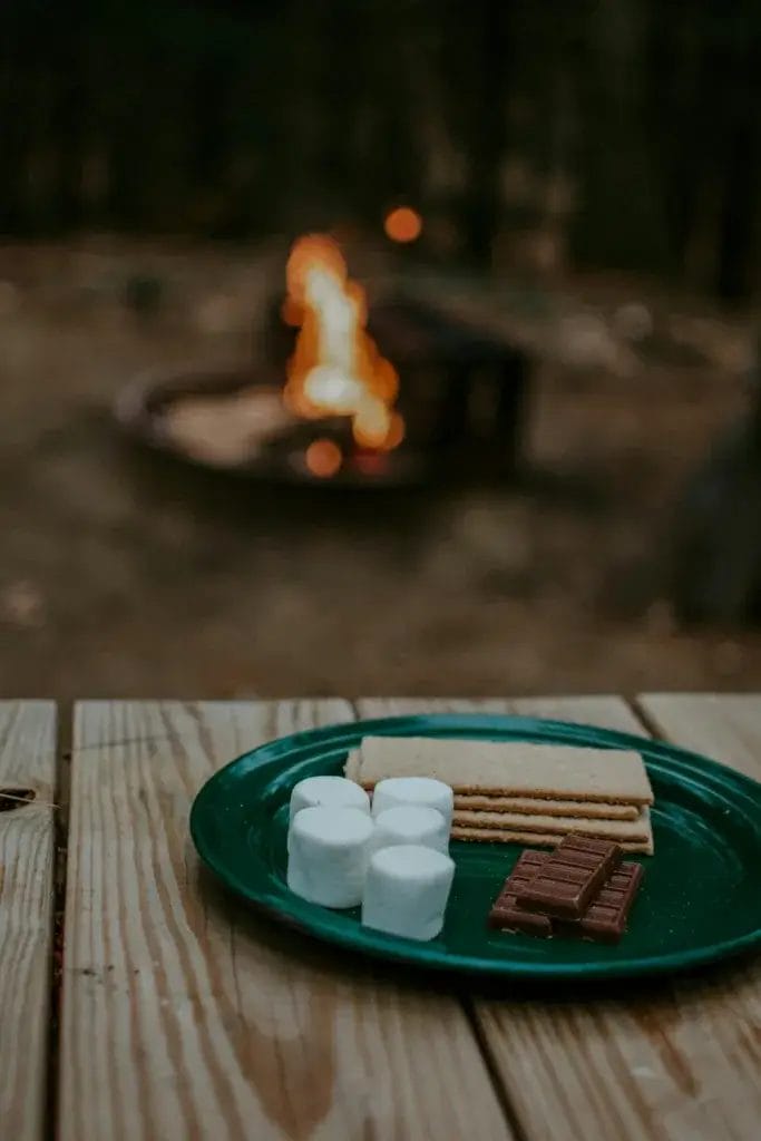 S'mores setup with marshmallows, graham crackers, and chocolate by a campfire.
