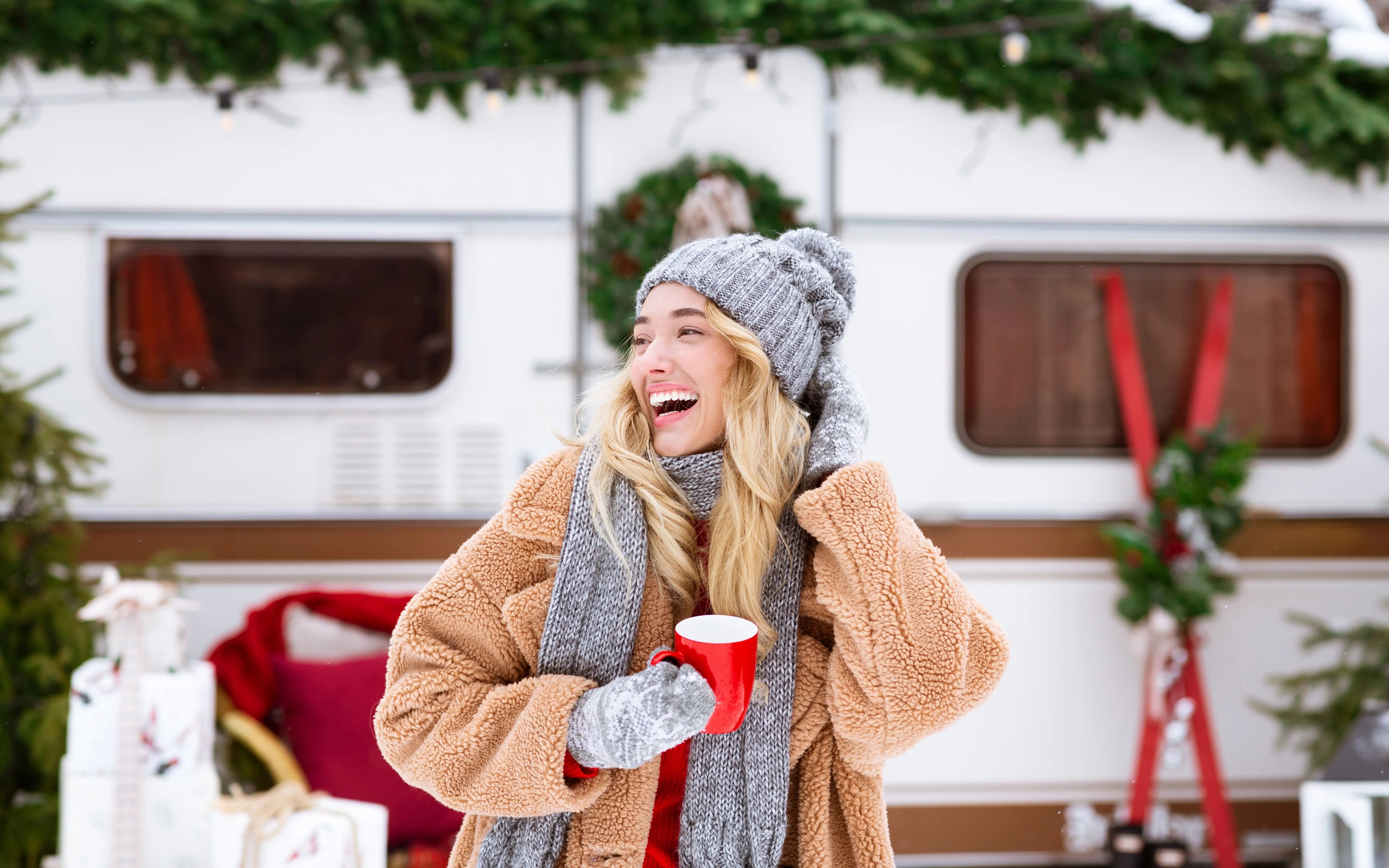 Woman christmas camping dressed in warm layers with festive decorations in the background.